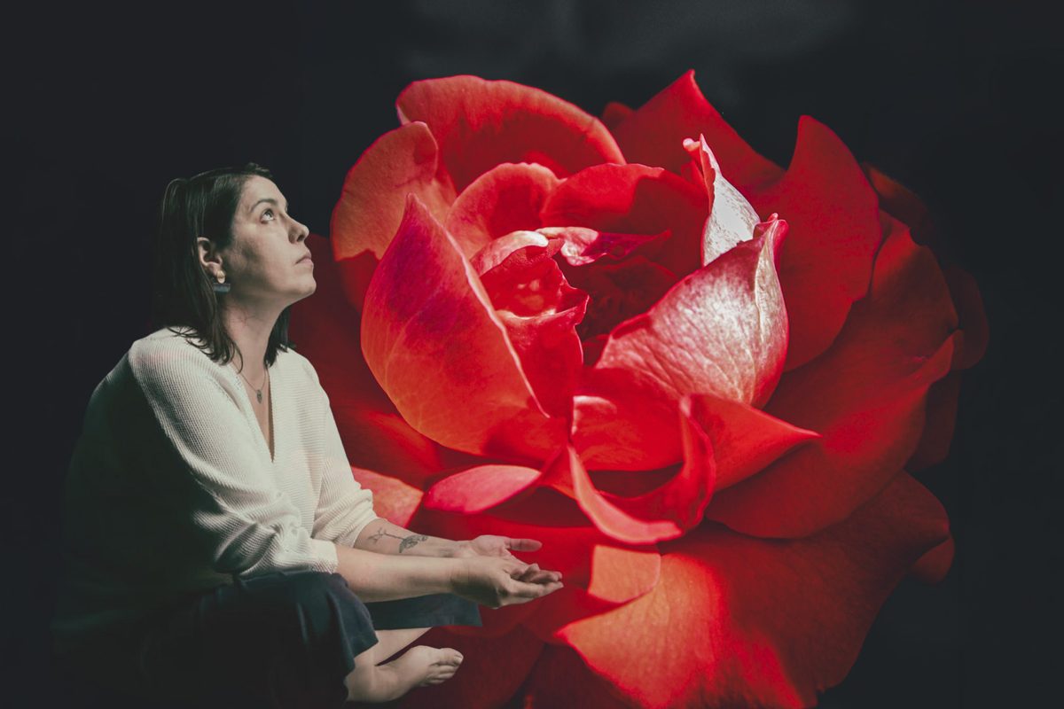 Cristina Rodrigues sentada junto a uma rosa vermelha, a olhar para cima